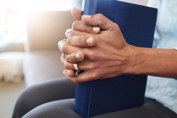 Book, prayer and hands of old woman in living room for religion, bible and Christian faith. Spiritu